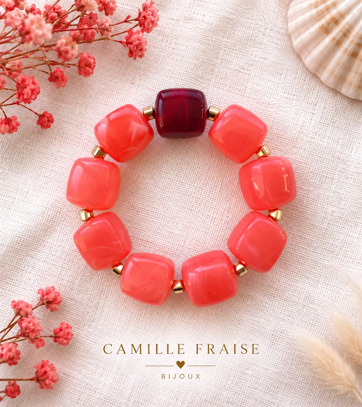 Bracelet de perles corail avec une perle bordeaux et séparateurs dorés, sur lin écru