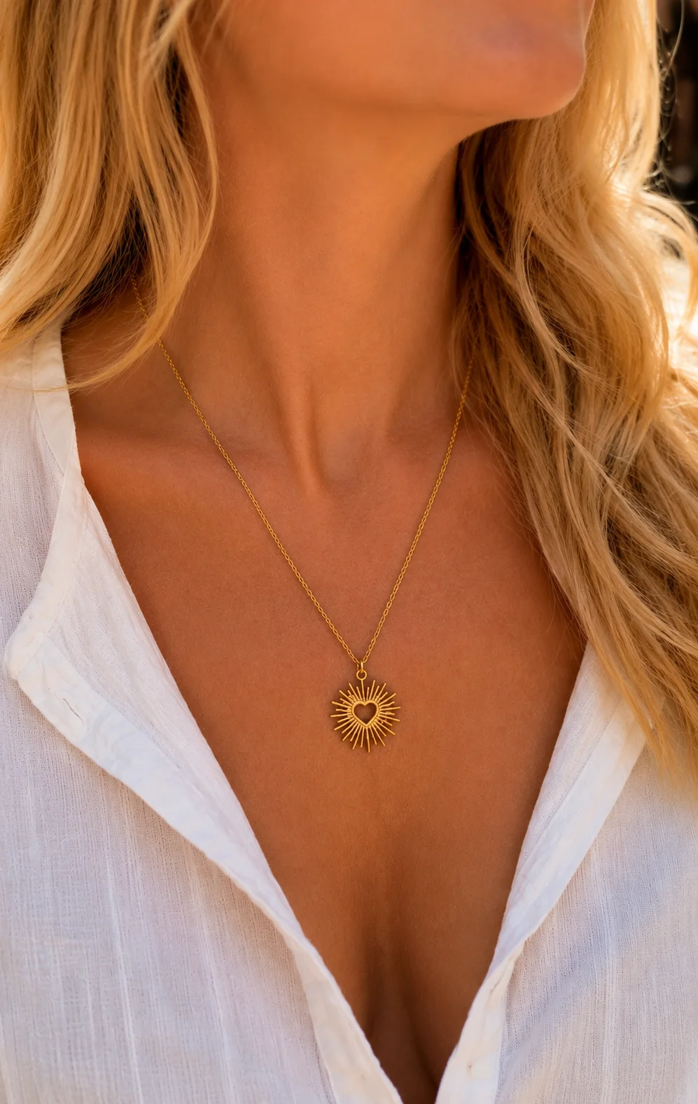 Collier doré avec pendentif cœur rayonnant porté sur une chemise blanche