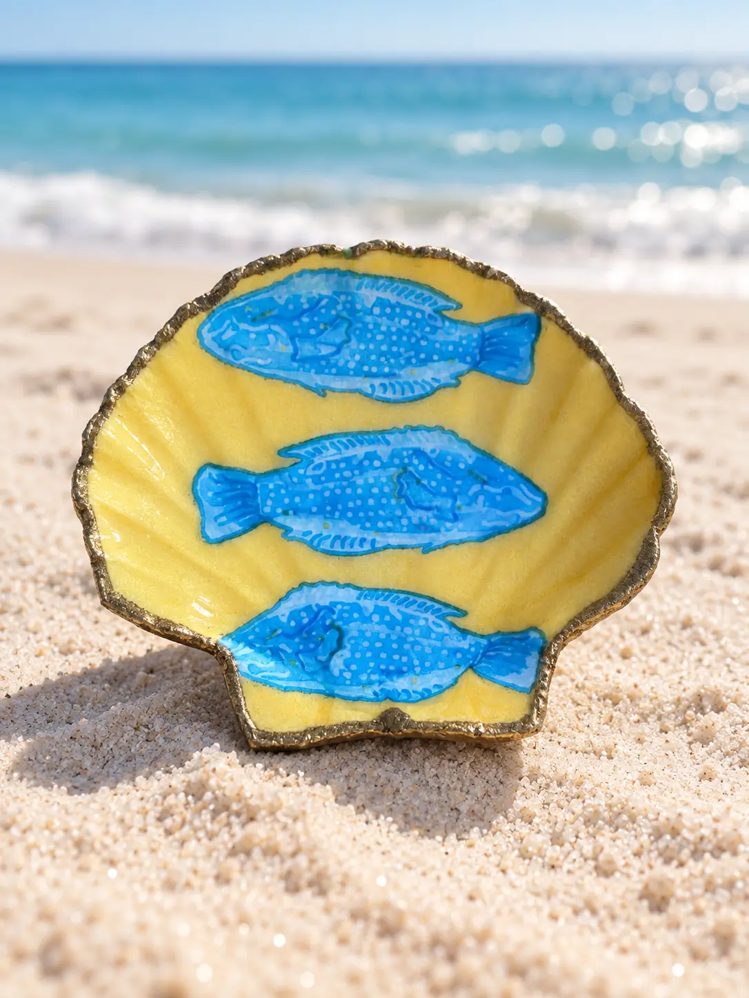 Coquille Saint-Jacques jaune soleil ornée de trois poissons bleus.